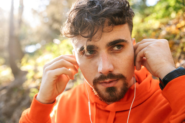 Handsome young sports fitness man runner outdoors in park listening music with earphones. - Foto, Imagen