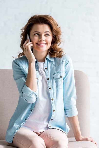 Kanepede oturan ve Grey smartphone cep telefonu ile konuşurken mutlu kıvırcık kadın  - Fotoğraf, Görsel