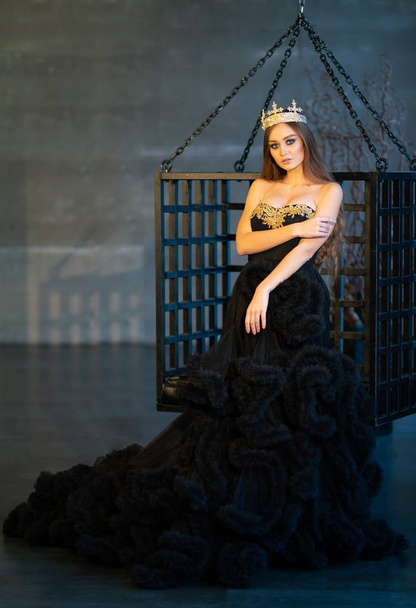 Model girl in a black dress and a crown on the background of the lattice - Foto, Imagen
