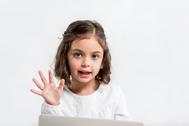 Смешной дошкольник машет рукой и смотрит на камеру, изолированную на белом
 - Фото, изображение