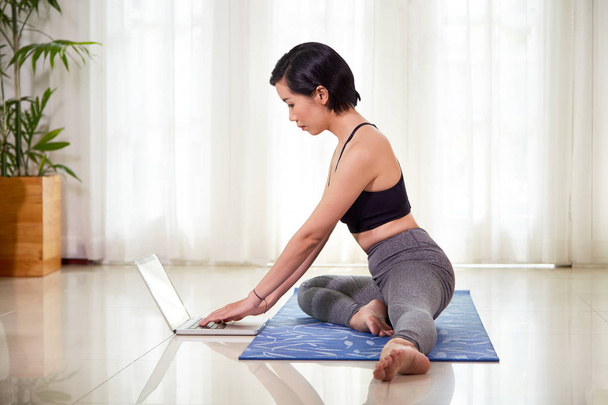 Fit Aziatische vrouw kijken tutorial over laptop thuis en het doen van yoga training - Foto, afbeelding