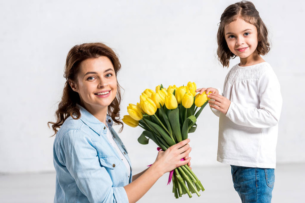 Happy mother holding bouquet of yellow tulips from daughter on white  - Foto, Imagen