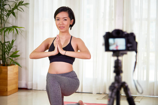 Blogger asiática sana en ropa deportiva haciendo yoga y filmando su entrenamiento en cámara como lección de aprendizaje
 - Foto, imagen
