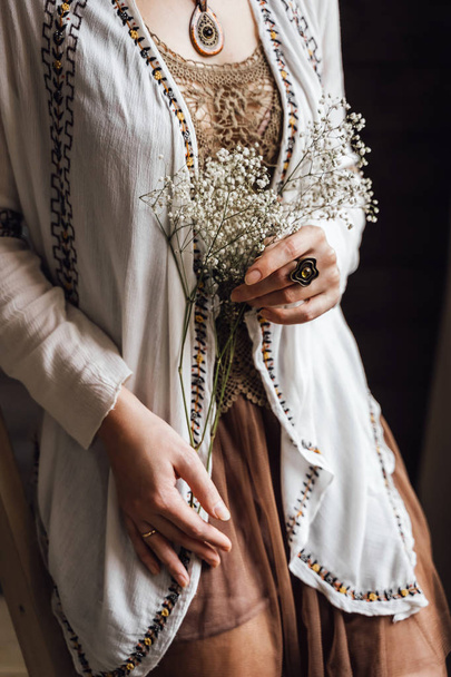 Ενότητα μέσα από την γυναίκα στην εκλεκτής ποιότητας λινό φόρεμα με κοσμήματα και μπουκέτο από άγρια λουλούδια - Φωτογραφία, εικόνα