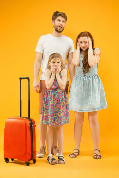 Sad parent with daughter and suitcase at studio isolated on yellow background - Foto, Imagem