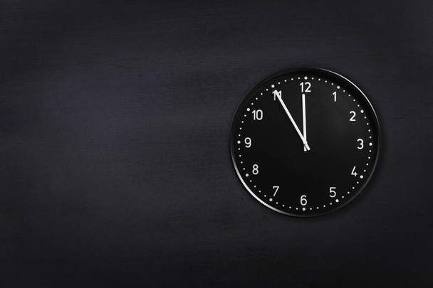 Horloge noire montrant cinq minutes à minuit sur fond de tableau noir. Horloge de bureau montrant 5 min à minuit ou midi
 - Photo, image