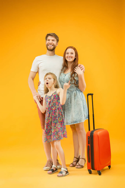 Happy parent with daughter and suitcase at studio isolated on yellow background - Fotoğraf, Görsel