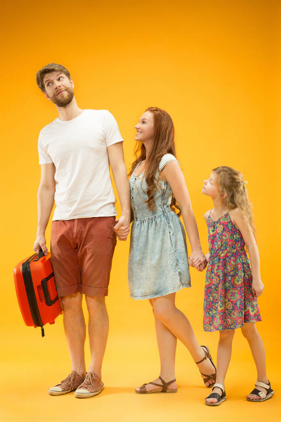 Happy parent with daughter and suitcase at studio isolated on yellow background - Foto, Imagem
