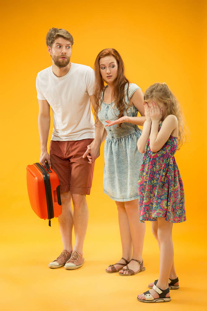 Sad parent with daughter and suitcase at studio isolated on yellow background - Fotó, kép