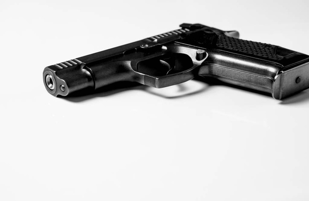 Чорний металевий пістолет лежить на білому тлі, крупним планом
 - Фото, зображення
