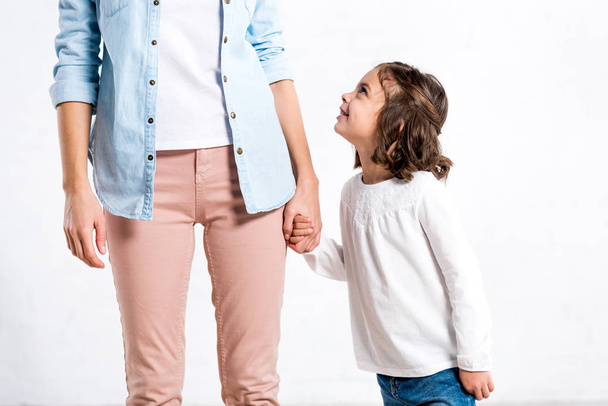 Partial view of woman in blue shirt holding hands with daughter on white  - Foto, Imagem