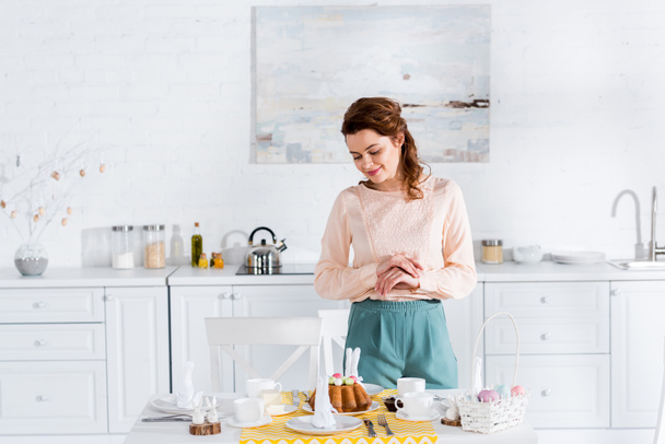 Happy woman looking at easter cake on table in kitchen - Foto, Bild