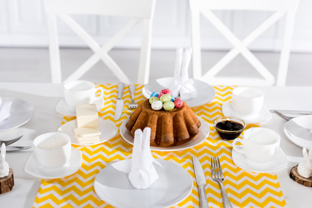 Pastel de Pascua con huevos pintados y vajilla en la mesa
 - Foto, Imagen