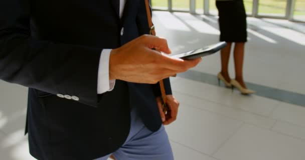 Mid section of a businessman walking in the office lobby while using his mobile phone  - Imágenes, Vídeo