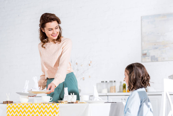 Charming woman looking at daughter with smile while decorating table  - Foto, afbeelding