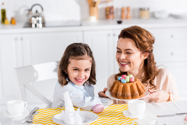 Laughing mother and daughter serving table with easter in kitchen - Photo, Image