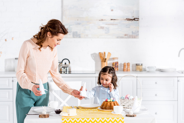 Vonzó nő ad lánya félbehajtott fehér szalvéta konyhában - Fotó, kép
