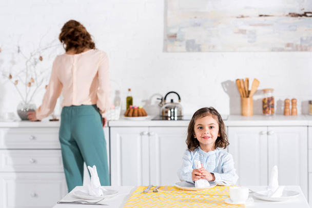 Радісна дитина сидить за столом і тримає білу серветку
 - Фото, зображення