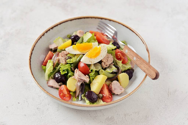 Francouzský salát Nicoise s tuňákem, vařené brambory, vejce, zelené fazolky, rajčata, sušené olivy, hlávkový salát a ančovičky. Pohled shora.  - Fotografie, Obrázek