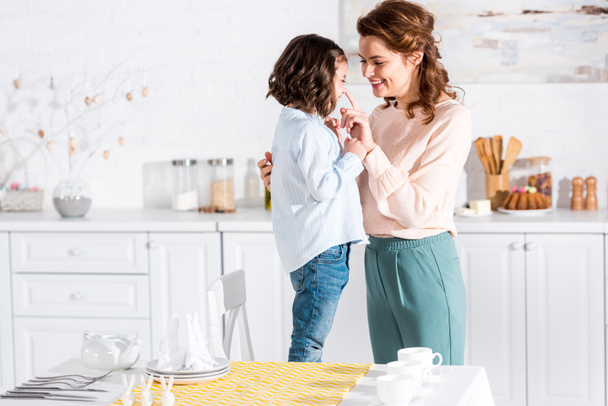 Smiling mother and child in kitchen near table with yellow tablecloth - Foto, afbeelding