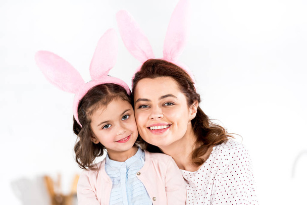 Smiling mother and daughter in bunny ears looking at camera on white  - Fotoğraf, Görsel