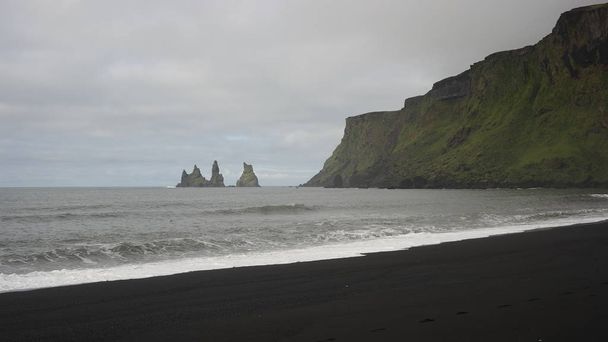 A view of Reynidrangar rocks, Reynisfjall cliff and black beach from Vk village on the south of Iceland - Fotoğraf, Görsel