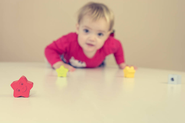 Schattige blonde meisje dragen rode jurk spelen met speelgoed aan tafel. - Foto, afbeelding