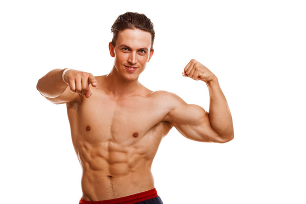 Handsome young ripped bodybuilder flexing his muscles smiling cheerfully pointing to the camera. Sexy athletic healthy man showing his biceps isolated, copy space. Gym, lifestyle, motivation concept - Foto, imagen