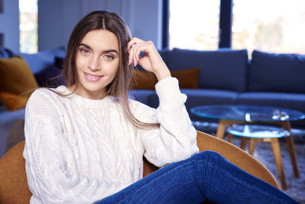 Portrait of beautiful young lady wearing casual clothes and smiling while relaxing on couch at home.  - 写真・画像