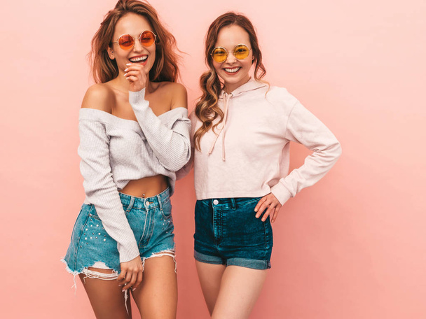 Two young beautiful smiling hipster girls in trendy summer hipster clothes. Sexy carefree women posing on pink background. Positive models having fun - Photo, Image
