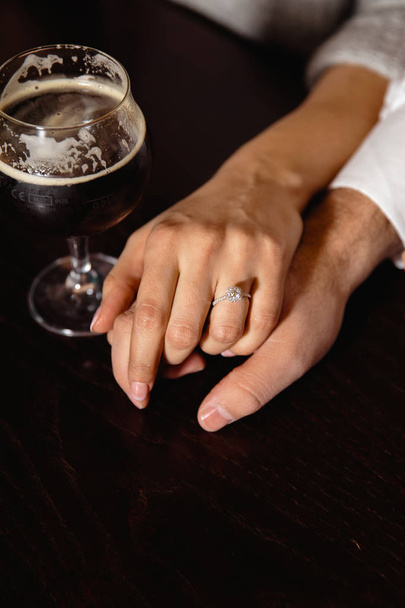 Heiratsantrag im wirklichen Leben: Paar hält Händchen in Kneipe mit einem Glas Bier an der Seite - Foto, Bild
