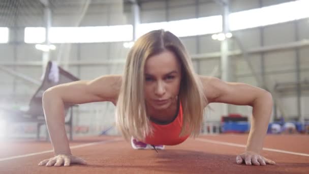 Kobieta lekkoatletycznego w stroje sportowe robi push up w hali sportowej - Materiał filmowy, wideo