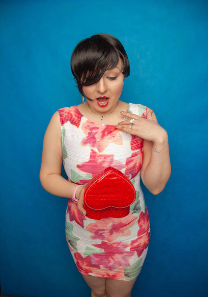 vrij gelukkig brunette met rood hart de doos van de gift van de vorm op blauwe studio effen achtergrond - Foto, afbeelding