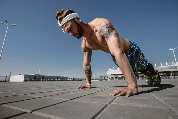 Handsome shirtless sportsman looking away doing push up exercise on workout ground outdoors at bright sunny day. Sport lifestyle - Photo, image