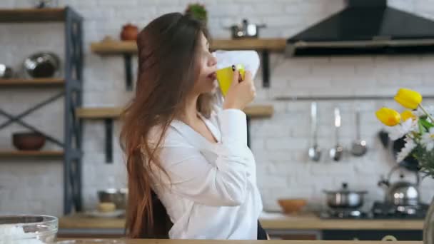 Young woman at the kitchen. Holding cup, smiling and looking at the camera. - Záběry, video