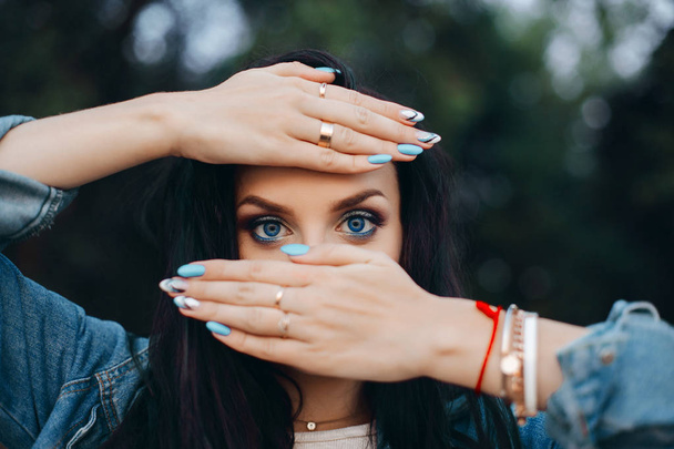 Pretty lady hiding behind hands with blue and white nails. - Photo, Image