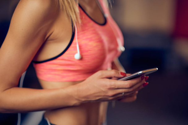 Close up de mulher usando telefone inteligente para mensagens de texto / leitura enquanto está de pé no ginásio. Conceito de estilo de vida saudável
. - Foto, Imagem
