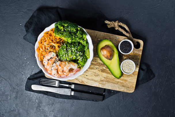 A bowl of balanced health food. Ingredients: shrimps, avacado, carrots, broccoli and rice. Black background, top view - 写真・画像