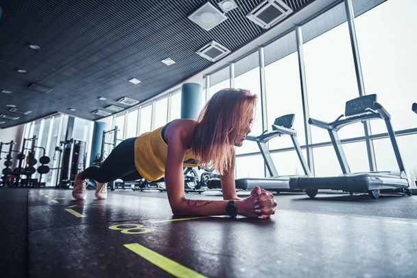 Стройная фитнес-женщина работает в современном спортзале, делает доску на коврике
 - Фото, изображение