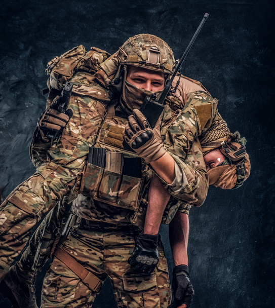 Des soldats des forces spéciales secourent son coéquipier blessé en le portant sur ses épaules depuis le champ de bataille, en parlant à la radio et en appelant au soutien
 - Photo, image
