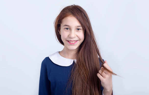Portrait of a happy girl on a light background. Schoolgirl in blue dress. - Photo, image