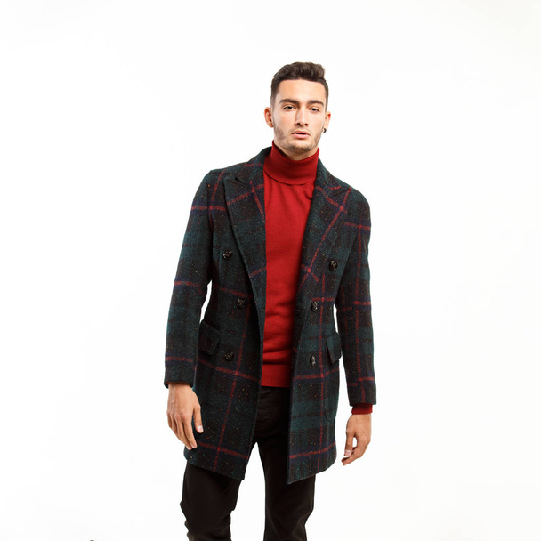 Young stylish man dressed in red turtleneck, brown pants and a plaid coat  stands on the white background - Fotoğraf, Görsel