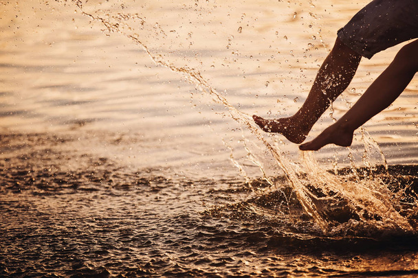 casal espirrando seus pés na água ao pôr do sol
 - Foto, Imagem