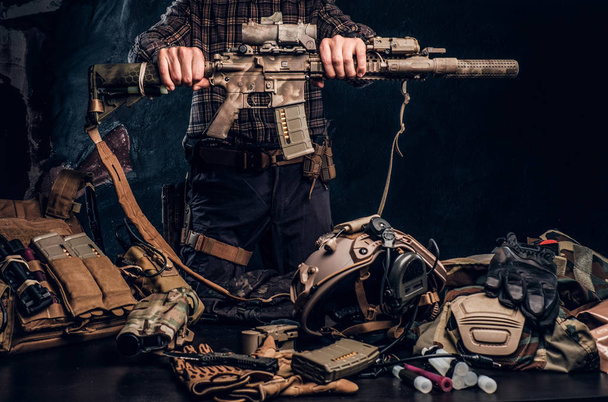Mann im karierten Hemd hält Sturmgewehr in der Hand und zeigt seine Militäruniform und Ausrüstung. moderne Ausrüstung für Spezialeinheiten. - Foto, Bild