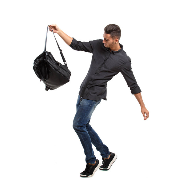 Young stylish man dressed in a black shirt and jeans poses with black backpack on the white background - Valokuva, kuva