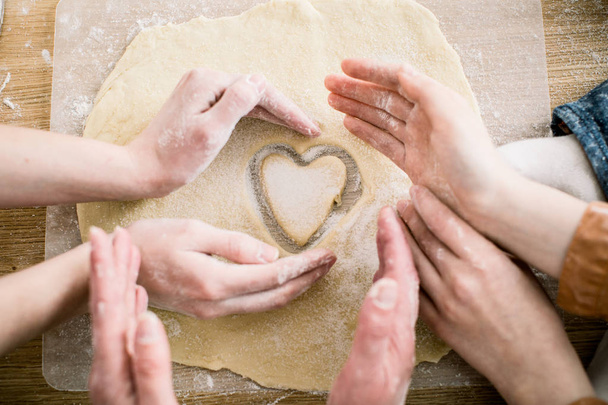 cooking and home concept - close up of female hands making cookies from fresh dough at home. Hands of three women hold cookie in form of heart - 写真・画像