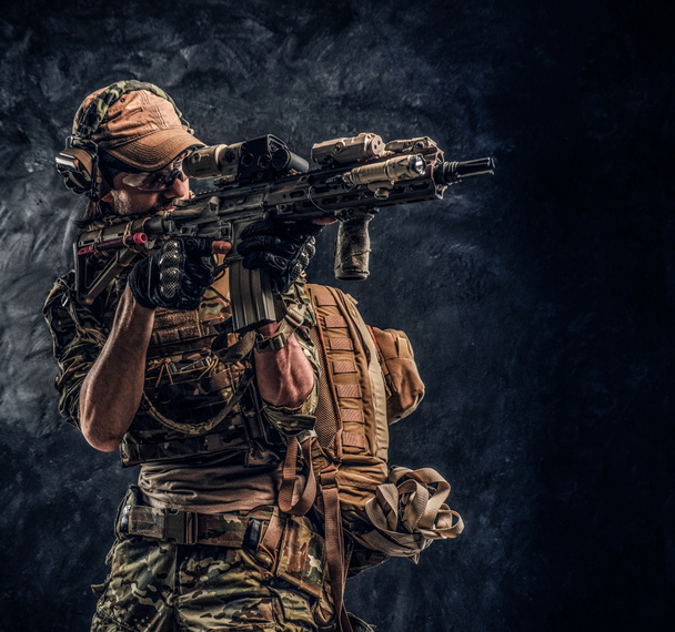 La unidad de élite, soldado de las fuerzas especiales en uniforme de camuflaje que sostiene un rifle de asalto con una mira láser y apunta al objetivo. Foto del estudio contra una pared oscura
   - Foto, imagen