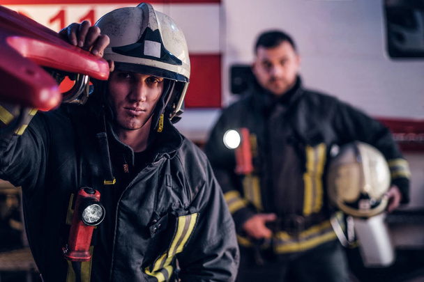 Два пожежники носять захисну форму, що стоїть поруч з пожежною машиною. Прибуття за викликом в нічний час
 - Фото, зображення