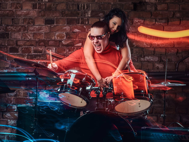 Girl hugs her idol who plays on a drum set in nightclub against a brick wall - Photo, Image