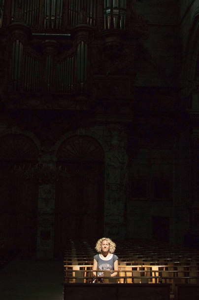 blondynka kręcone kobieta siedzi samotna w ciemnym kościele w sunbeam - Zdjęcie, obraz
